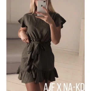 Grön klänning volanger AFJ x NA-KD - Mörkgrön volangklänning, omlott med knytdetalj från AFJ x NA-KD. Jättefint skick, storlek 36. ⚡️ 