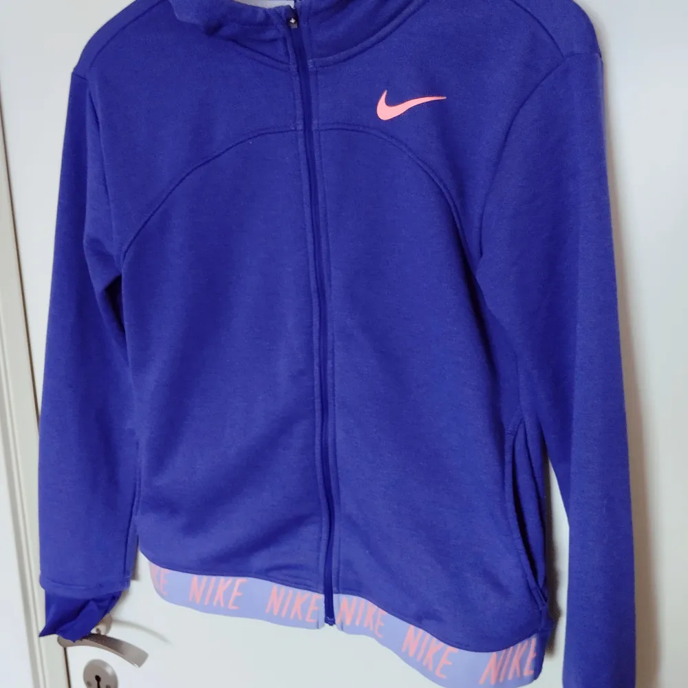 Nike Girls' G Nk Dry Hoodie Fz Studio Jacket i härlig lila färg med detaljer i rosa. !! OBS!! PÅ STORLEKEN! (se bild) Storleken är XL men för 13-15 år. Använd fåtal gånger pga fel storlek. Nypris 550kr. Säljes för 300kr. . Hoodies.