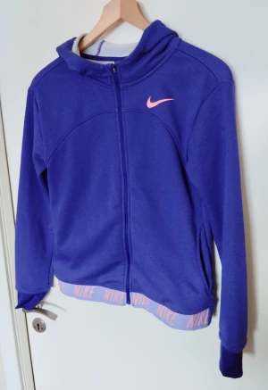 Nike Girls' G Nike Girls Dry Hoodie Fz Studio Jacket (XL)  - Nike Girls' G Nk Dry Hoodie Fz Studio Jacket i härlig lila färg med detaljer i rosa. !! OBS!! PÅ STORLEKEN! (se bild) Storleken är XL men för 13-15 år. Använd fåtal gånger pga fel storlek. Nypris 550kr. Säljes för 300kr. 