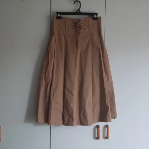 Midikjol med korsettdetalj - Beige midikjol med korsett i midjan. Den är benad och prdentligt öglad, så man kan dra åt den trots att det inte är en "riktigt" korsett. Den har fickor.