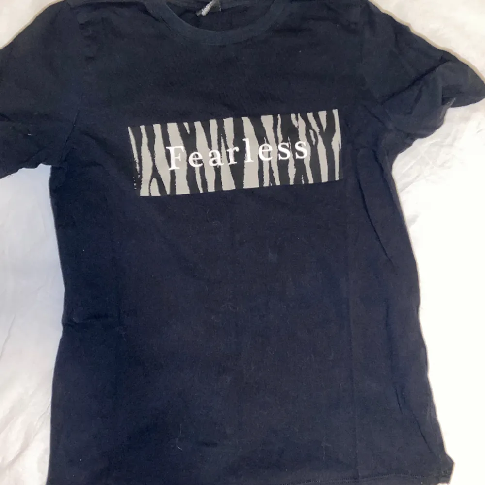 Säljer en svart T-shirt med zebratryck. På tröjan står det ”Fearless”, från ginatricot i storlek S. Knappt använd. OBS: köparen står för frakten. (Annonsen finns ute på fler sidor.). T-shirts.