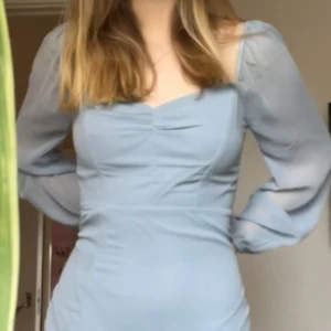 Ljusblå midiklänning med slits!  - Endast använd en gång och är bristfri! Har en lång fin slits till övre låret och långa ärmar i genomskinligt tyg. Stängs med en dragkedja på ryggen eftersom tyget ej är så stretchigt. 