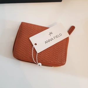 Ny plånbok från Anna Field - Plånbok från Anna Field, helt oanvänd med prislappen kvar. Är 15 cm lång och 10 cm bred. Har ett stort fack för sedlar. Ett fack med dragkedja för mynt. Åtta fack för kort, plus 2 innerfack. Nypris på Zalando var 130 kr.