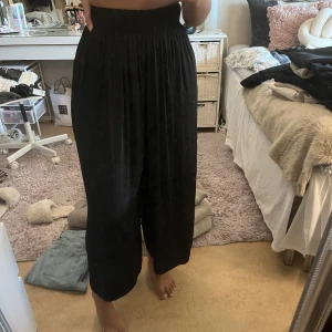 Svarta vida byxor i satin - Ett par högmidjade vida byxor köpt från Lindex. Jätte sköna och fina. Croppad form, i satin material. I st XS. Aldrig använda 