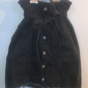 Svart Jeanskjol - Denna svarta jeanskjolen har ett bälte i midjan som är löstagbart och knappar längs hela framsidan. Den är extremt stretchig och går lika bra att klä upp som klä ner.