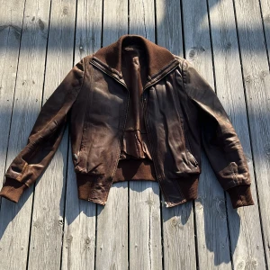 Brun skinnjacka - Brun skinnjacka med krage och tajt passform. Har två ytterfickor och tre innerfickor. Finns två små hål (en vid kragen och en vid ena ärmen)