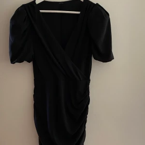 Draperad svart klänning  - Figurnära klänning perfekt V-ringning. Puffärmar. Draperat tyg. Kort modell.  Använd 2ggr. 