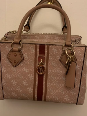 GUESS - Väska från Guess i bra material, använd 1 gång. Bra med fack i, finns också ett långt band till