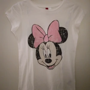 Vit topp med medvetet slitet Minnie Mouse tryck. Strlk: 34, XS. Lite defekt. - Vit topp med medvetet slitet Minnie Mouse tryck fram och bak i ryggen. Strlk: 34, XS. Bomull. Lite defekt då den fått lite  blå ton på vissa ställen, troligen från blåa nya jeans eller liknande som färgat av sig i en låda. Går förhoppningsvis bort i tvätt