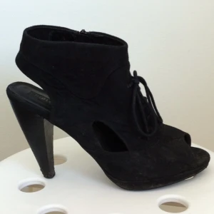 Svarta skor med klack och knyt framtill. Mockaliknande material. Klack ca 8 cm. - Svarta skor med klack och knyt framtill. Mockaliknande material. Klack ca 8 cm.