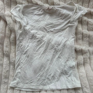 Vit v-ringad topp från Nelly - Säljer en enkel och söt vit topp från Nelly i storlek S. Toppen har v-ringning med spetskant och är kortärmad. Tillverkad i mjuk bomull, perfekt till sommaren. Passformen är normal och toppen är lätt att matcha med olika stilar.