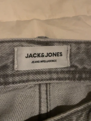 Grå loose fit jeans från Jack & Jones - Säljer ett par ljusgrå jeans från Jack & Jones i modellen Loose/Chris. De har en loose passform och raka ben, klassisk femficksdesign och är tillverkade i mjukt jeanstyg. Perfekta om du gillar en avslappnad och trendig stil.