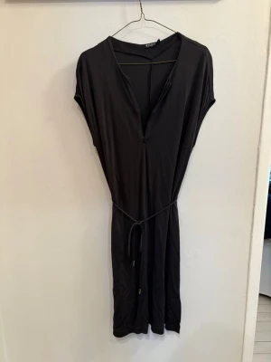 Svart kortklänning från Tiger of Sweden - Svart kortklänning med v-ringning och knytband i midjan från Tiger of Sweden. Klänningen har en enkel och stilren design med ärmlös passform och mjukt, följsamt material som känns skönt mot huden.