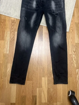 Svarta Dsquared2 - Säljer ett par svarta jeans från Dsquared2 med snygga slitningar och tvättade detaljer på framsidan. Jeansen har raka ben, klassiska bakfickor och en cool Dsquared2-label bak. Materialet är jeans och passformen är normal.