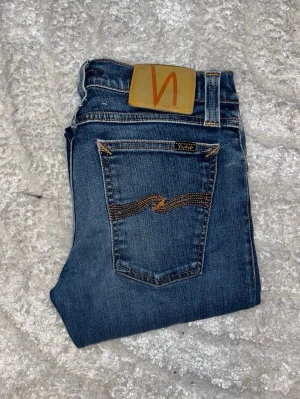 Nudie jeans  - Snygga skinny jeans från Nudie Jeans som skiftar i olika blå. OBS storlekslappen saknas med jag skulle uppskatta till W26 L30 -  men utgå efter mått. Midja 34cm, längd 99cm. JAG SKICKAR EJ FLER BILDER NÄR JAG BÄR JEANSEN! för bättre inblick i passformen rekommenderar jag att googla på modellnamnet. För storleksguide kolla måtten noggrant då jeansen alltid kan vara uppsydda heller krympta och jag ej tar emot returer :) s6,1