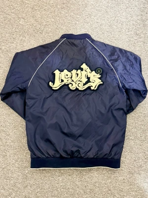 Vintage Levi's bomberjacka Red Tab - Vintage mörkblå bomberjacka från Levi's Red Tab med broderad logga i teddy på ryggen med en vintage/y2k still. Helt ny, hör av dig vid frågor eller behov av fler bilder!☺️