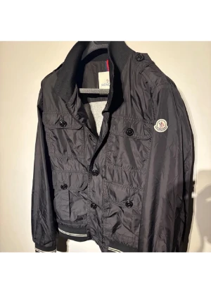 Svart vindjacka från Moncler - Säljer en svart vindjacka från Moncler. Skick alldeles utmärkt, förutom knapp som lostnat (bild 4)! Pris ej HUGGET i sten! Hör av er vid frågor eller funderingar!