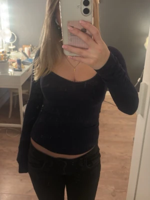 Svart långärmad topp med spetskant - Säljer en svart långärmad topp med v-ringad urringning och fin spetskant längs halsen. Toppen har en tight passform och är gjord i ett mjukt, stretchigt material som sitter snyggt på kroppen. Perfekt att styla med jeans eller kjol.