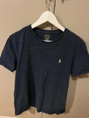 Mörkblå t-shirt från Polo Ralph Lauren - Snygg mörkblå t-shirt från Polo Ralph Lauren med klassisk rund hals och den ikoniska vita logon broderad på bröstet. Tillverkad i mjuk bomull och har en enkel, stilren design som passar till allt.
