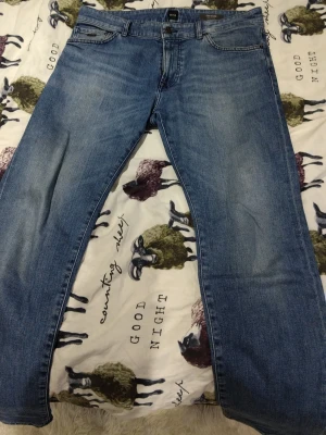 Blå jeans från BOSS - Säljer ett par klassiska blå jeans från BOSS, modell 030 MAINE Regular Fit. Jeansen har fem fickor, bälteshällor och snygga slitningar för en avslappnad look. Materialet är jeans i bomull och passformen är rak och normal. Riktigt sköna då de har den så kallade stretch möjligheten. 