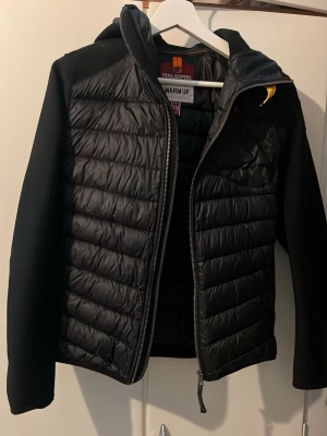 Svart pufferjacka från Parajumpers - Säljer en svart pufferjacka från Parajumpers med quiltad front och ärmar i mesh-liknande material. Jackan har dragkedja framtill, en bröstficka med dragkedja och klassisk PJS-patch på ärmen. Perfekt för dig som vill ha en stilren och sportig look.