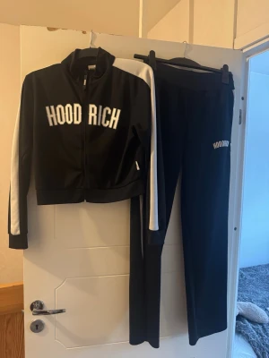 HOODRICH tracksuit - Säljer ett svart sett från HOODRICH med vita ränder längs tröjan och byxorna. Settet har en sportig look med tydlig HOODRICH-logga på bröstet och är gjord i ett sportigt material som är bekvämt. Äkta vara! 
