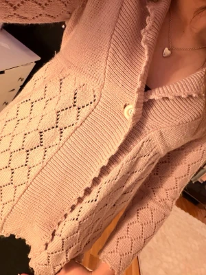 Ljusrosa stickad kofta från Lindex - Supersöt ljusrosa stickad kofta från Lindex med ett snyggt hålmönster i diamantform. Koftan har en  krage, en knapp framtill och vågiga kanter. Perfekt att slänga på sig över en topp när det är lite kyligt ute. Stilren och söt🥰 aldrig använd, säljs pga att den inte kommer till användning💞💞