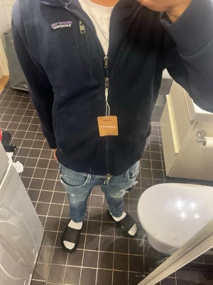 Mörkblå fleeceväst från Patagonia  - Säljer en mörkblå fleeceväst helt ny  från Patagonia i storlek S. Västen har aldirg använts. Klassisk Patagonia-logga på bröstet och mjukt fleecematerial som är perfekt för lager-på-lager. Enkel och stilren design.