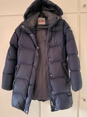 Mörkblå McKinley pufferjacka med huva - Säljer en mörkblå pufferjacka från McKinley med stor, mysig huva och dragkedja framtill. Jackan har quiltad design, sidofickor och McKinley-logga på ärmen. Perfekt för kalla dagar och riktigt skön att bära.