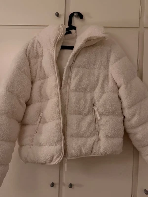 Vit teddyjacka från Everest - Mysig vit teddyjacka från Everest med huva och dragkedja framtill. Jackan har två fickor med dragkedja och en fluffig, quiltad look. Perfekt för kalla dagar när du vill vara både varm och stylish.