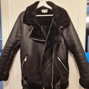 Svart aviator jacka från NA-KD - Svart aviator jacka med bälte nertill och detaljer i silver. Supersnygg med boots till hösten. Använd 1 gång och har blivit hängandes i garderoben. 