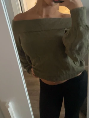 Olivgrön offshoulder stickad tröja - Säljer en olivgrön stickad tröja med offshoulder-design och långa ärmar. Tröjan har ribbade muddar vid ärmslut och nederkant, vilket ger en snygg och avslappnad look. Perfekt för dig som vill ha en trendig och bekväm stil.