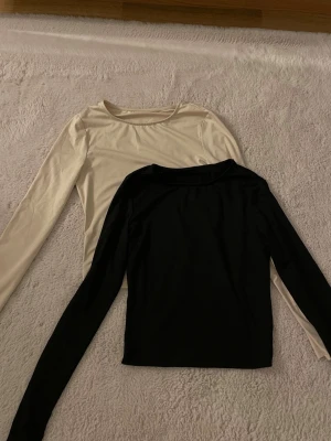 2 cropped toppar, svart och beige - Två snygga långärmade toppar från Shein i svart och beige, båda med rund halsringning och cropped design. Den beige är lite mer av ett träningsmaterial och stretchig, medan den svarta är mjuk och följsam som en vanlig topp. Perfekta basplagg att styla med jeans, kjol eller under jackor och koftor. Storlek XS/S.