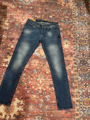 Blå skinny jeans från Dondup - Säljer ett par blå skinny jeans från Dondup med klassisk femficksdesign och snygga slitningar på låren. Jeansen har gul kontrastsöm och en läderpatch bak i midjan. Materialet är jeans med en mjuk känsla och passformen är tight hela vägen ner.