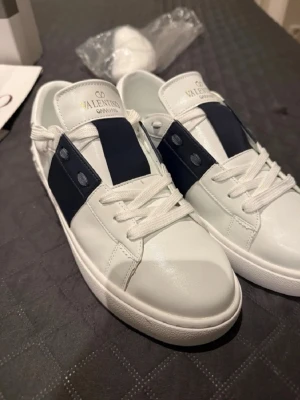 Valentino Garavani vita sneakers - Snygga vita sneakers från Valentino Garavani🤩.Skorna har rund tå, platt sula och är gjorda i skinn. Perfekta för dig som vill ha en clean och lyxig look🌟. skorna är nästintill helt oanvända, fick i present