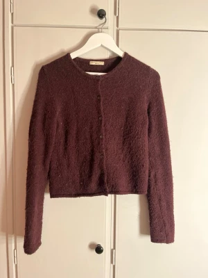 Mörk vinröd kofta från Gina Tricot - Mysig mörk vinröd kofta från Gina Tricot i fluffigt stickat material. Koftan har rund halsringning, långa ärmar och knäppning framtill med små knappar. Perfekt för lager-på-lager under hösten och vintern.