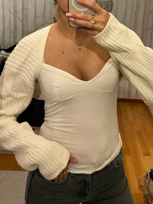 Vit bolerotopp i stickat - Säljer en vit bolerotopp i ribbstickat material med långa ärmar. Toppen är perfekt att slänga över ett linne eller en tight topp. Supermjuk och skön, passar till de mesta! 