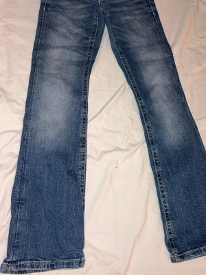 Blå bootcut jeans Gina Tricot 146 - Snygga blå jeans från Gina Tricot i storlek 146. Bootcut-modell med broderade detaljer och paljetter på bakfickan samt en dekorativ knapp. Klassisk tvättad jeanslook och normal passform. Perfekta för dig som gillar lite extra detaljer på dina jeans. 