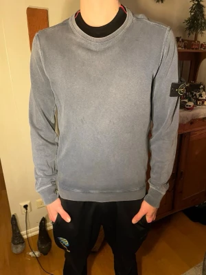 Blå Stone Island tröja med patch - Säljer en blå långärmad tröja från Stone Island med  patchen på vänster ärm. Tröjan har rund hals och är gjord i mjuk bomull. Jäkligt snygg men samtidigt väldigt stilren!