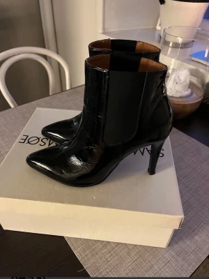 Svarta lackstövletter från Samsøe Samsøe - Säljer ett par svarta stövletter i glansigt lackmaterial från Samsøe Samsøe. Skorna har spetsig tå, hög klack och elastiska paneler på sidorna för enkel påtagning. Helt nya. Nypris 1500 kr. Storlek 40 men passar även 39 då skon är liten i storleken. 