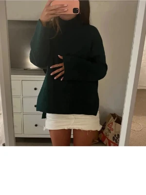 Mörkgrön stickad polotröja - Säljer en mörkgrön stickad polotröja med loose passform och långa ärmar. Tröjan har hög krage och är perfekt för kyliga dagar. Materialet är mjukt och ger en skön känsla. Enkel och stilren design som funkar till många olika outfits.