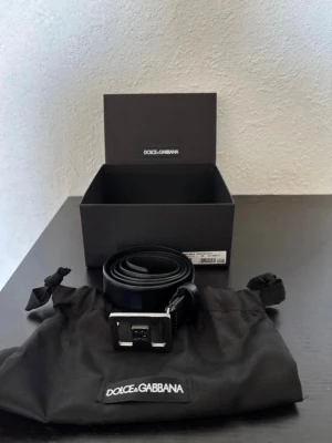 Svart skärp från Dolce & Gabbana - Säljer ett svart skärp från Dolce & Gabbana i äkta skinn med en silverfärgad metallspänne och DG-logga framtill. Skärpet kommer med originalpåse och box samt tags. Perfekt accessoar för att lyfta din outfit.