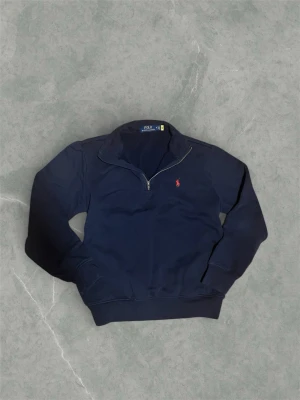 Marinblå half zip från Polo Ralph Lauren - Säljer en snygg marinblå half zip från Ralph Lauren. Den är i Storlek M men kan även passa en större S. Den är i fint skick utan några defekter. Har fungerande QR kod som tar dig till produkten på Ralph laurens hemsida. Vid några frågor eller funderingar är det bara att höra av sig.