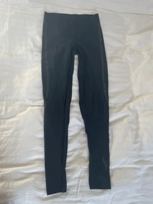Tränings leggings - Säljer ett par svarta leggings från Casall Sculpture med snygga blanka detaljer längs sidorna och snörning i midjan. De är tighta och har hög midja, perfekta för träning eller chill. Materialet är stretchigt syntet som sitter skönt.