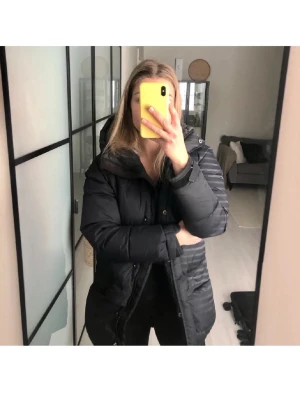 Svart lång pufferjacka Peak Performance - Säljer en svart lång pufferjacka från Peak Performance medellen snowline j med huva och stora fickor framtill. Jackan har dragkedja och knappar, samt en klassisk quiltad look. Perfekt för kalla dagar och riktigt skön att bära. Liknar fjällräven jackorna