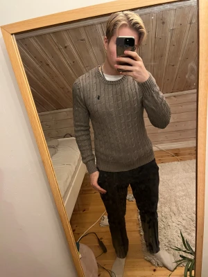 Beige kabelstickad tröja Polo Ralph Lauren - Säljer en beige kabelstickad tröja från Polo Ralph Lauren med rund halsringning och broderad logga på bröstet. Tröjan har lång ärm och ribbade muddar, perfekt för lager-på-lager under hösten och vintern.