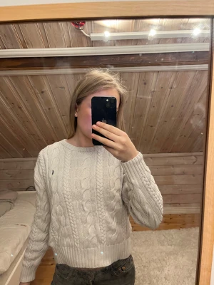 Vit stickad tröja från Polo Ralph Lauren - Säljer en klassisk vit kabelstickad tröja från Polo Ralph Lauren. Tröjan har rund halsringning, lång ärm och den ikoniska lilla broderade loggan på bröstet. Perfekt till jeans eller kjol för en clean och stilren look.