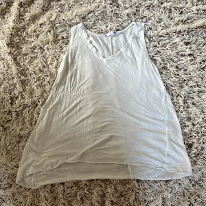 Vit linne från Lager 157 - Säljer en vit, ärmlös linnetopp från Lager 157 i storlek M. Toppen har v-ringning och tunna axelband, perfekt för varma dagar. Tillverkad i 100% viskos/viscose och har en enkel, flowy passform. Passar snyggt till jeans eller shorts. Det finns tyvärr små fläckar och några små hål.