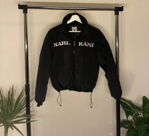 Pufferjacka  - Svart pufferjacka från Karl Kani i storlek XS men passar även S. Jackan har broderad logga i vitt framtill, dragkedja och snörning i nederkant. Den har en loose passform och är tillverkad i syntetmaterial. Brodering är sliten i stilen alltså inte på grund av brukning. 