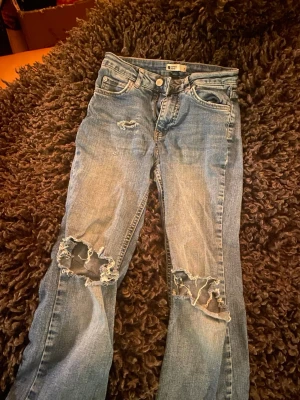 Blå ripped jeans från Perfect Jeans - Snygga blå jeans från Perfect Jeans i storlek S med slitna och trasiga detaljer på knäna och vid fickan. Klassisk femficksmodell med dragkedja och knapp. Jeansen har en rak passform och är tillverkade i jeansmaterial med ljus tvätt.